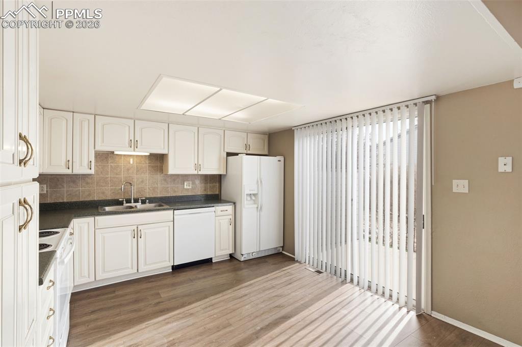 Kitchen featuring white appliances, dark countertops, wood-type flooring, and white cabinetry