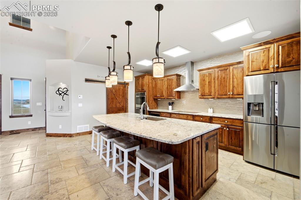 Kitchen with stainless steel appliances, a barn door, wood finish cabinetry, stone tile floors, and light stone counters