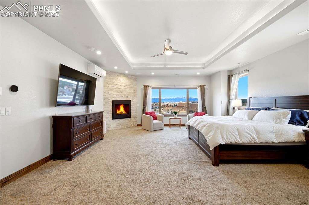 Bedroom with a fireplace, a ceiling fan, light carpet, a tray ceiling, and recessed lighting