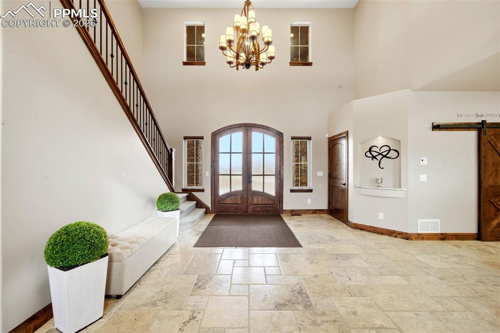 Foyer entrance with a barn door, stone tile floors, suspended lighting, french doors, and a high ceiling