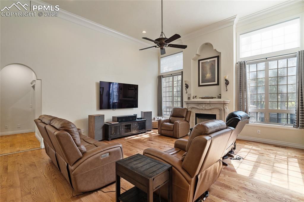 Living room with crown molding, a fireplace, light wood-style floors, a ceiling fan, and recessed lighting