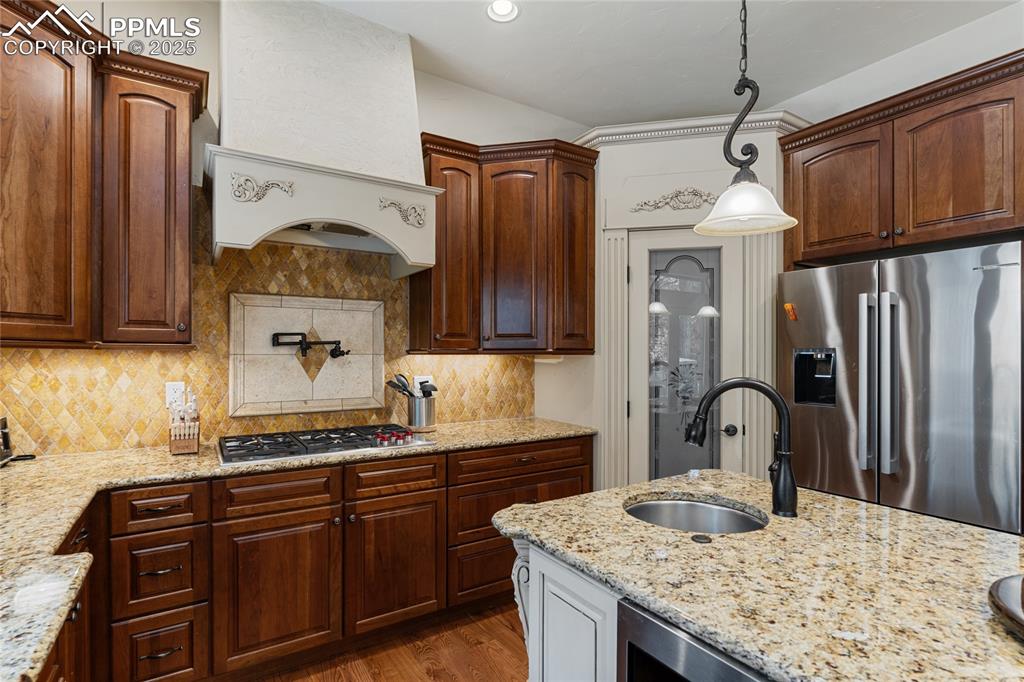 Kitchen featuring appliances with stainless steel finishes, light stone counters, white cabinetry, hanging light fixtures, and backsplash