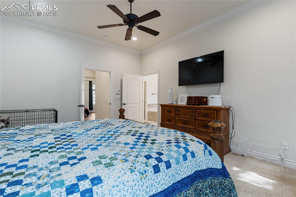 Carpeted bedroom featuring ornamental molding, ensuite bath, and ceiling fan