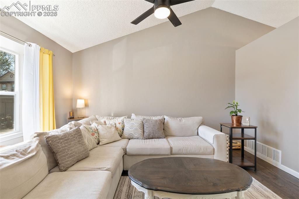 Living area featuring lofted ceiling, wood finished floors, a textured ceiling, and ceiling fan