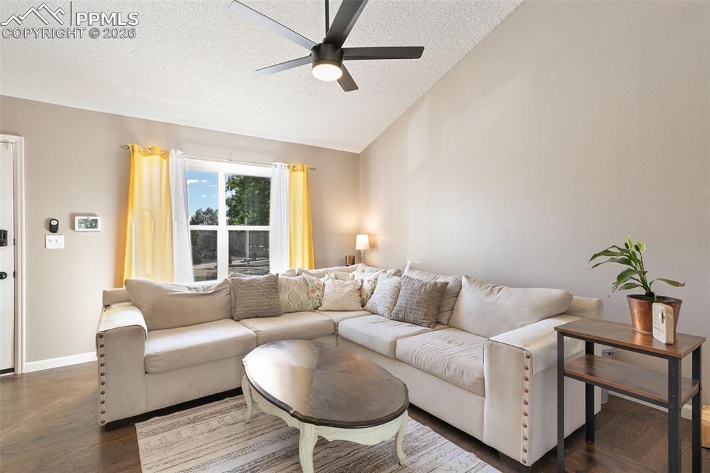 Living area with a textured ceiling, wood finished floors, lofted ceiling, and a ceiling fan