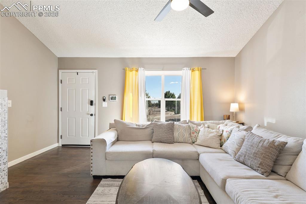 Living area featuring dark wood-style flooring, a textured ceiling, and ceiling fan