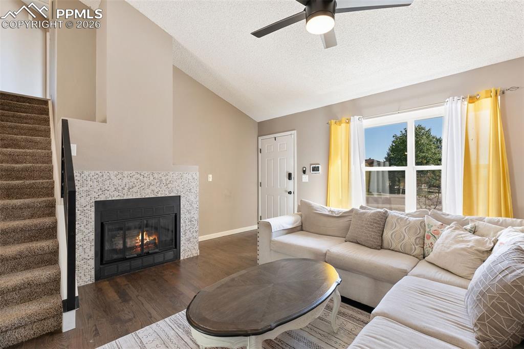 Living room featuring lofted ceiling, wood finished floors, stairs, a tile fireplace, and a textured ceiling