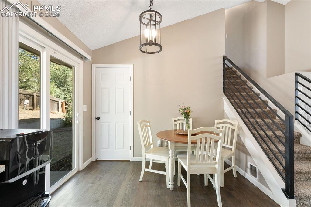 Dining space with wood finished floors, lofted ceiling, a textured ceiling, a chandelier, and stairway