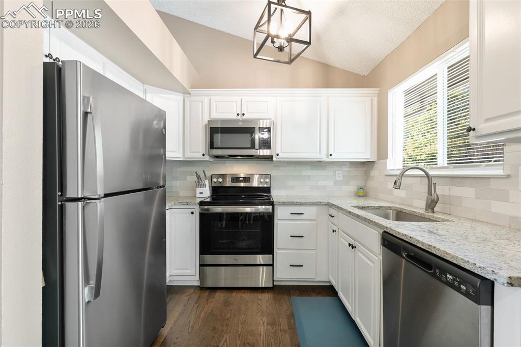 Kitchen with appliances with stainless steel finishes, light stone counters, lofted ceiling, backsplash, and white cabinets
