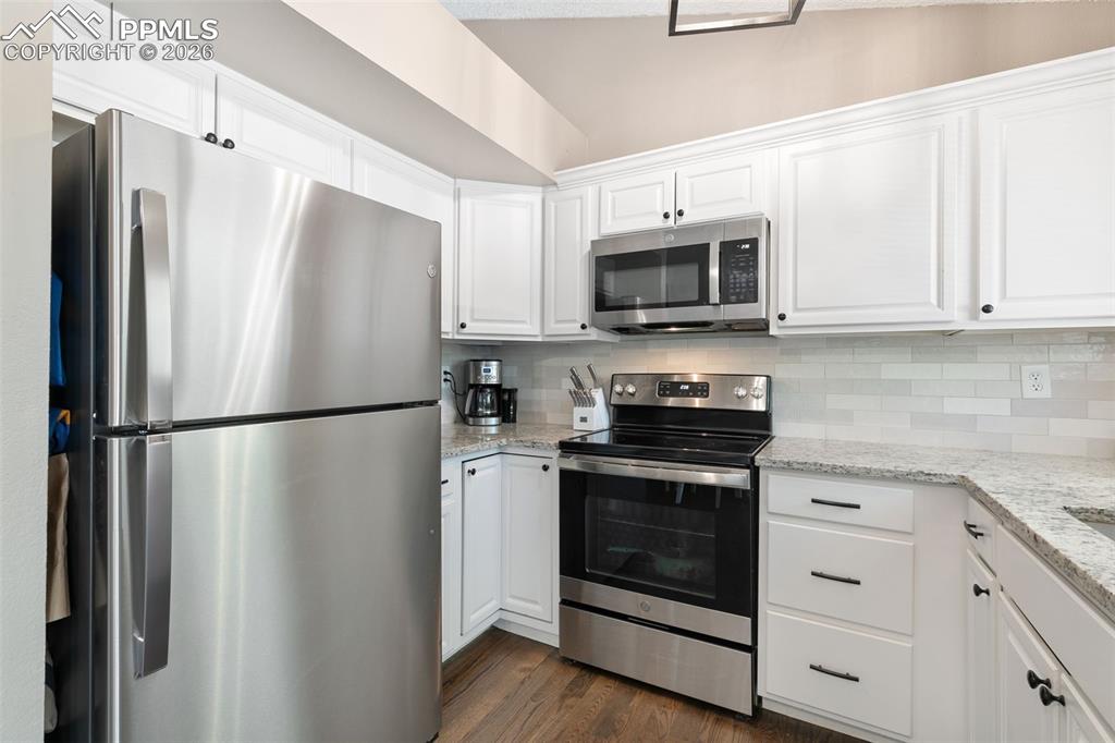 Kitchen with stainless steel appliances, white cabinets, light stone counters, and dark wood finished floors