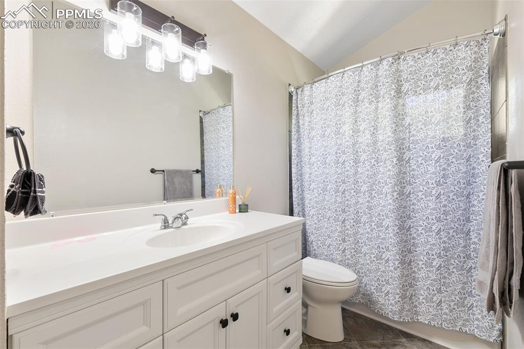 Bathroom with vanity, lofted ceiling, dark tile patterned floors, and curtained shower