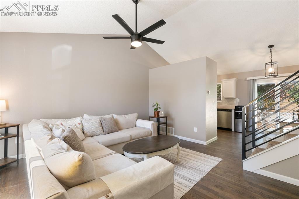 Living area featuring stairway, dark wood-style flooring, vaulted ceiling, and a ceiling fan
