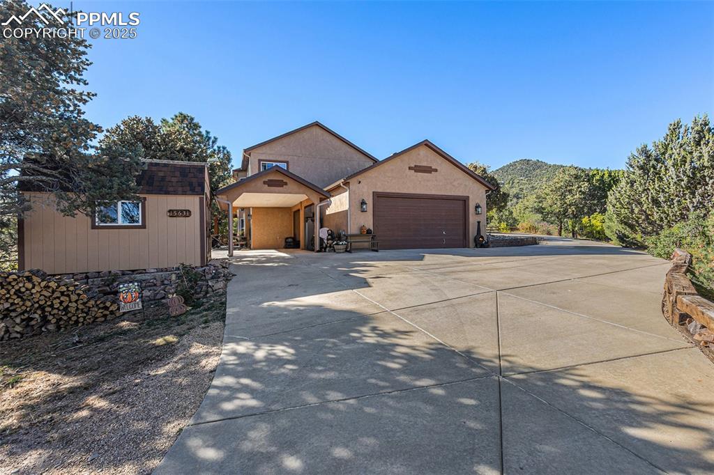 View of front of property featuring driveway, stucco siding, an outbuilding, and an attached garage