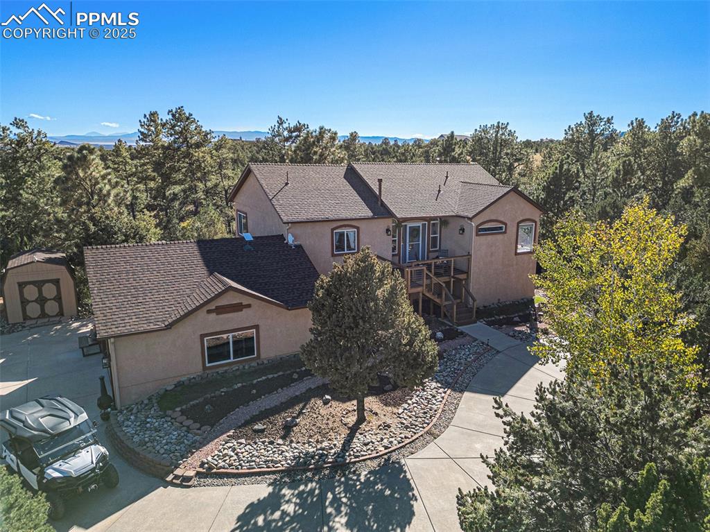 View of front of house featuring a wooden deck, stucco siding, a shingled roof, and an outbuilding