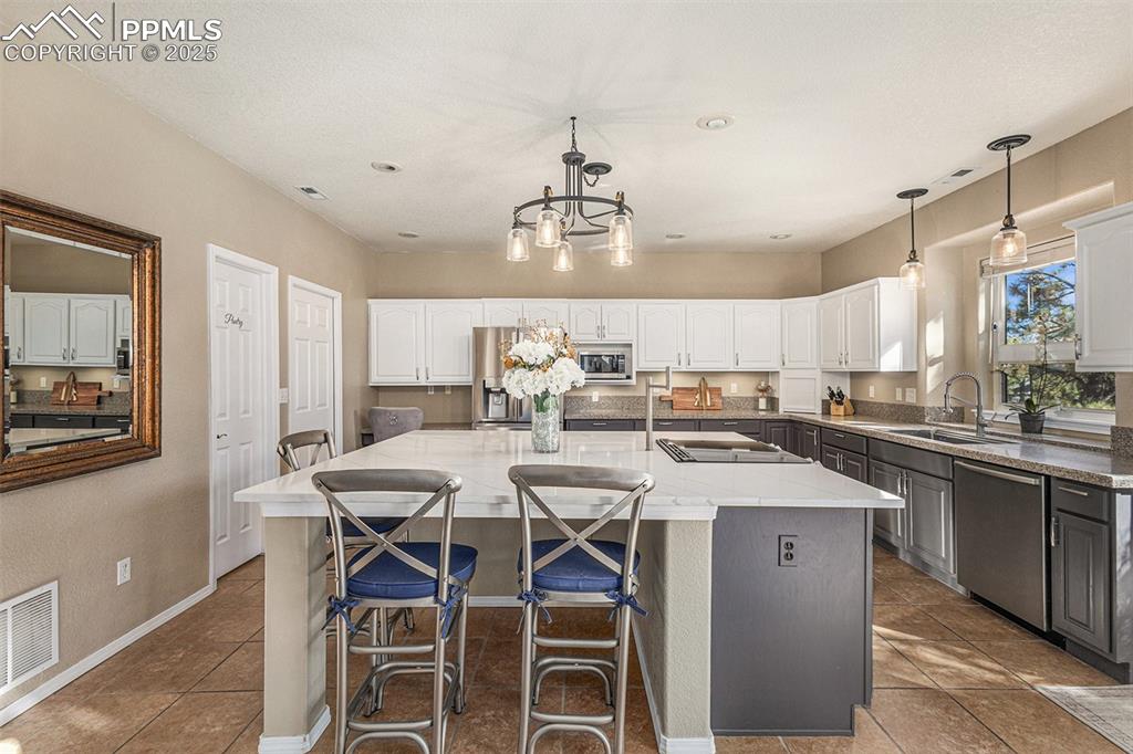 Kitchen featuring hanging light fixtures, appliances with stainless steel finishes, gray cabinetry, and white cabinets