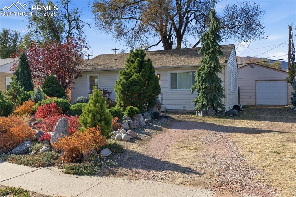 View of property hidden behind natural elements featuring an outbuilding, a detached garage, a shingled roof, and driveway
