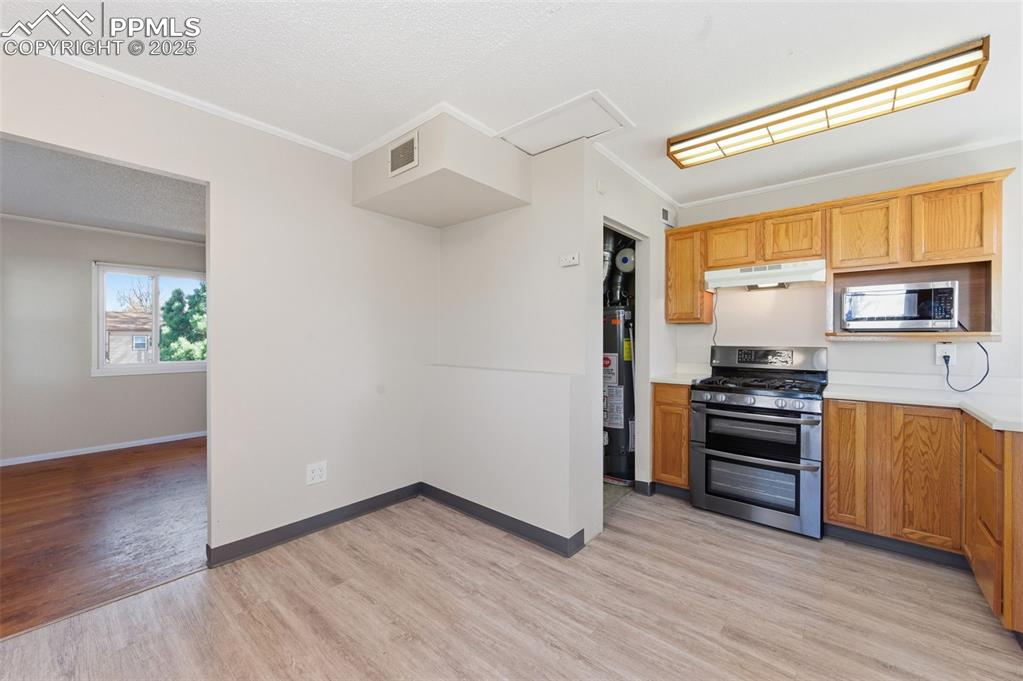 Kitchen with light countertops, appliances with stainless steel finishes, crown molding, light wood-style floors, and a textured ceiling