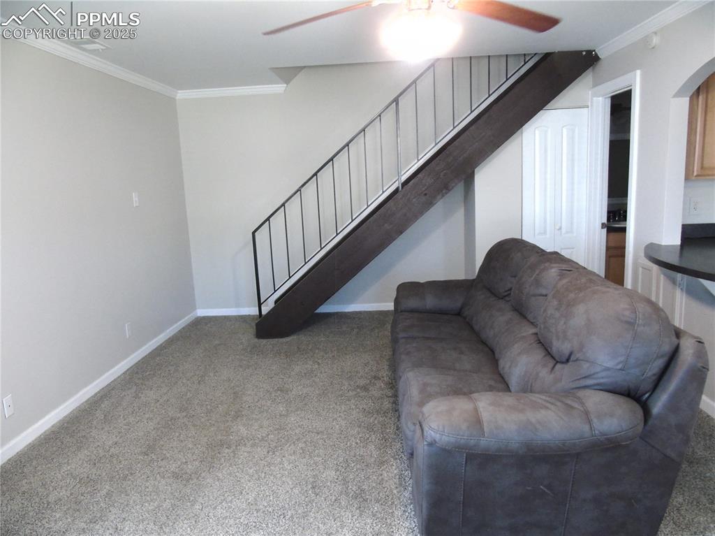 Living room featuring crown molding, ceiling fan, light colored carpet, and stairs
