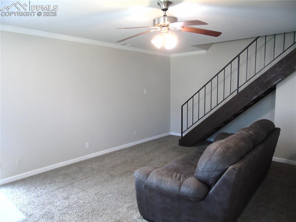 Carpeted living area with crown molding, a ceiling fan, and stairway