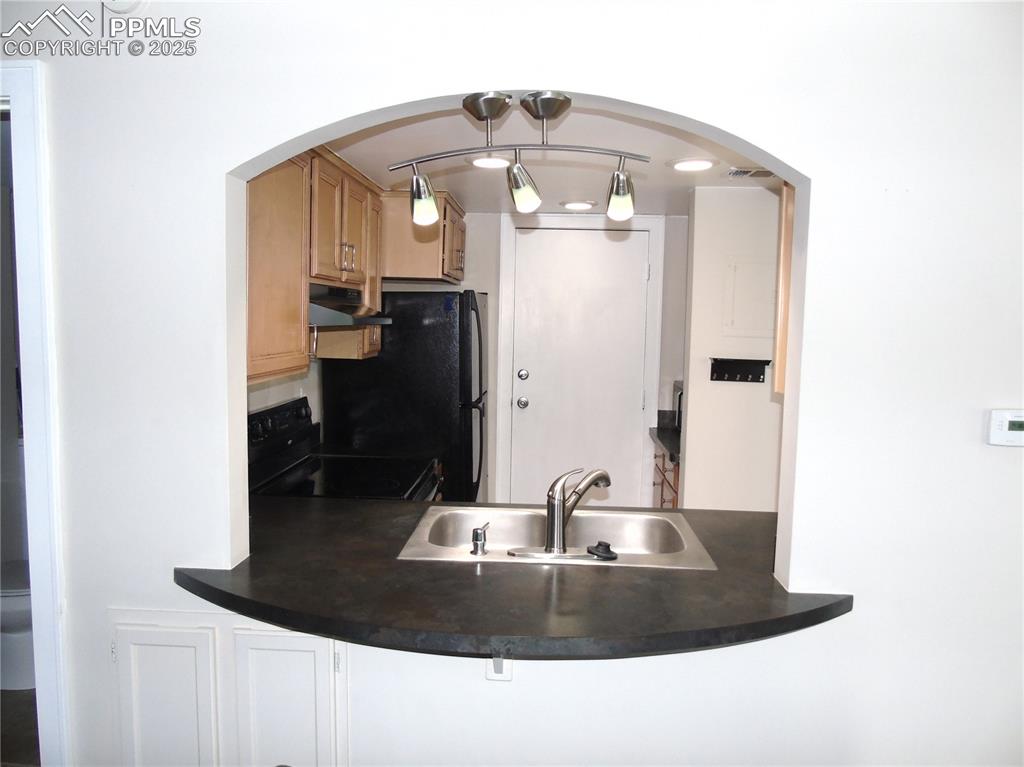 Kitchen with black appliances, pendant lighting, dark countertops, under cabinet range hood, and arched walkways