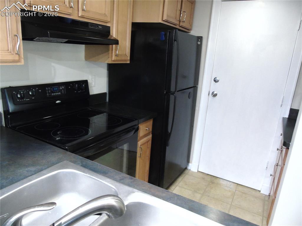 Kitchen with dark countertops, black electric range, under cabinet range hood, and light tile patterned floors