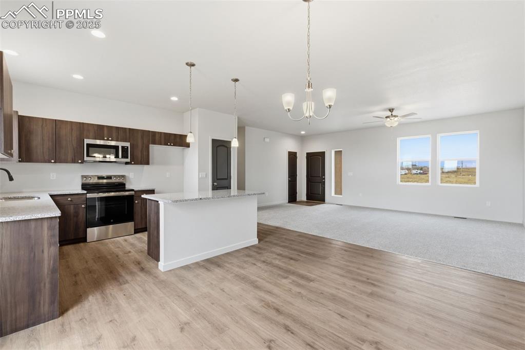 Kitchen featuring a chandelier, decorative light fixtures, stainless steel appliances, open floor plan, and light stone counters