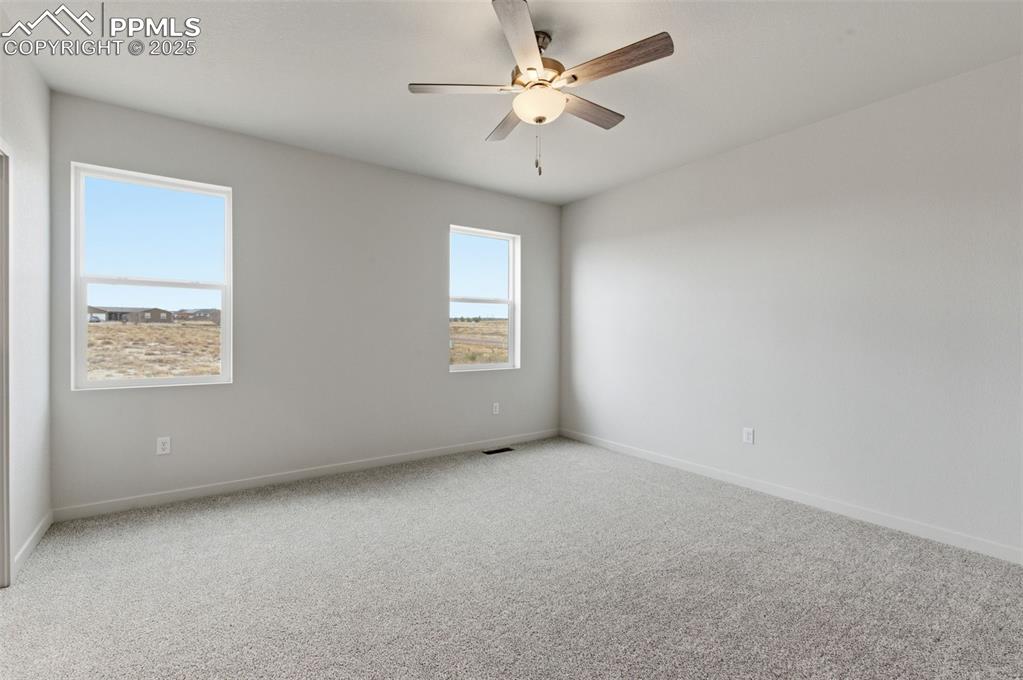 Carpeted empty room featuring ceiling fan and baseboards