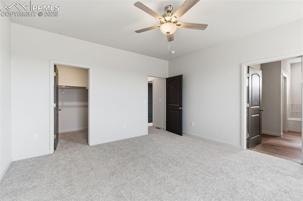 Unfurnished bedroom featuring a walk in closet, ensuite bath, light colored carpet, and a ceiling fan