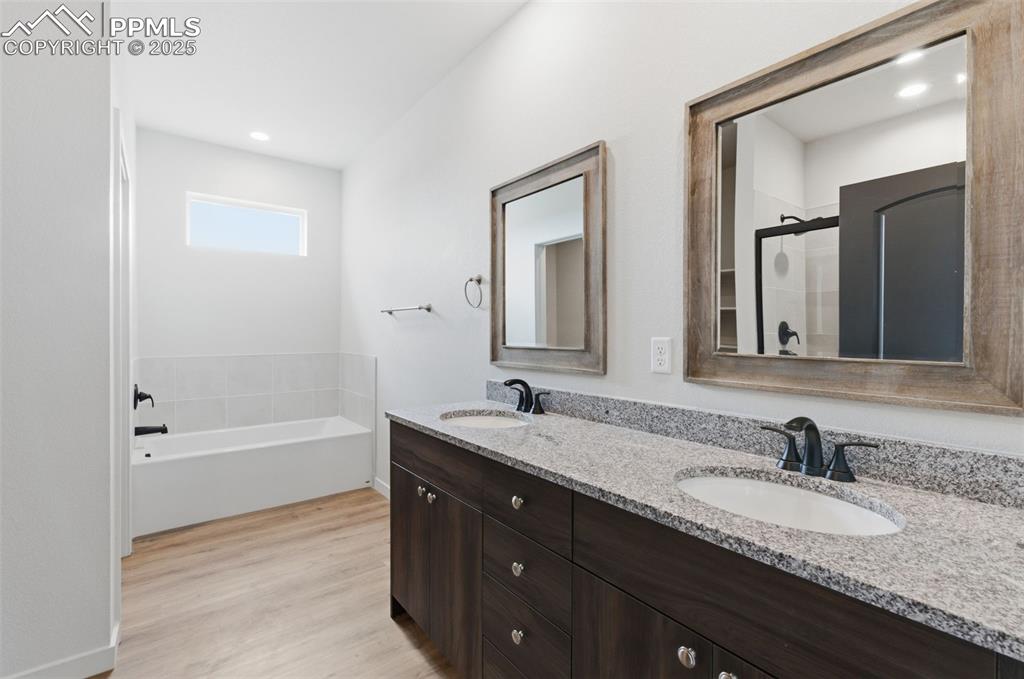 Full bathroom with double vanity, light wood-style floors, a shower stall, a bath, and recessed lighting
