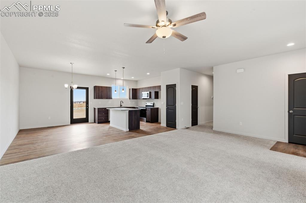 Unfurnished living room featuring light carpet, recessed lighting, a chandelier, and a ceiling fan