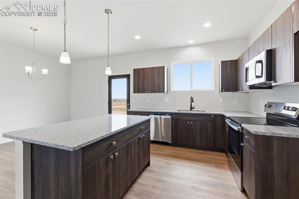 Kitchen featuring appliances with stainless steel finishes, dark brown cabinetry, light wood-type flooring, a kitchen island, and recessed lighting