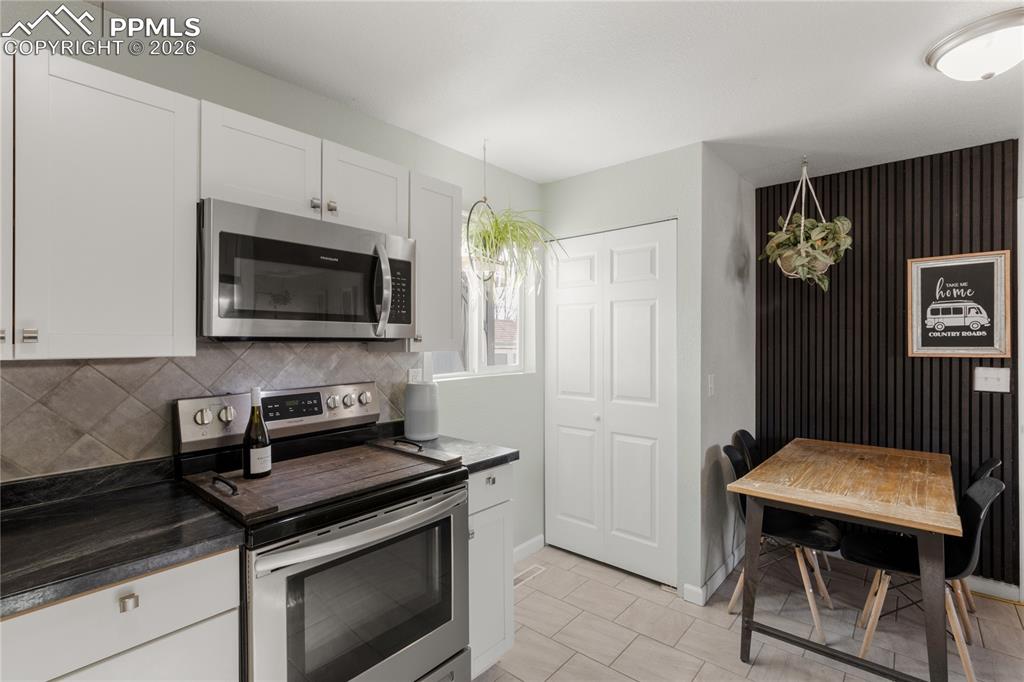 Kitchen featuring appliances with stainless steel finishes, dark countertops, white cabinets, decorative light fixtures, and decorative backsplash