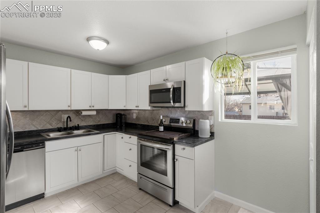 Kitchen with appliances with stainless steel finishes, white cabinetry, dark countertops, decorative light fixtures, and backsplash