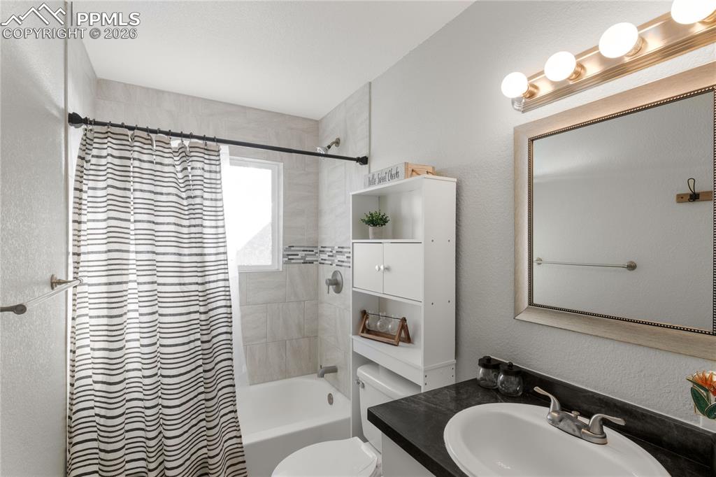 Full bath with a textured wall, shower / bath combo with shower curtain, and vanity