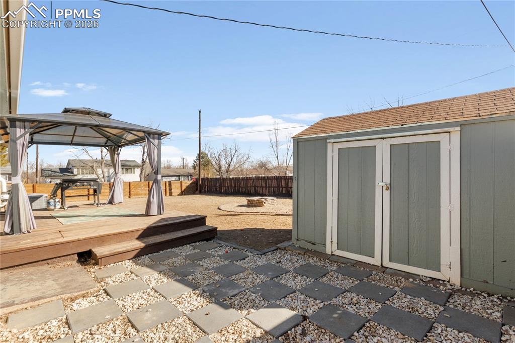 Fenced backyard with a gazebo, a storage unit, a wooden deck, and a fire pit