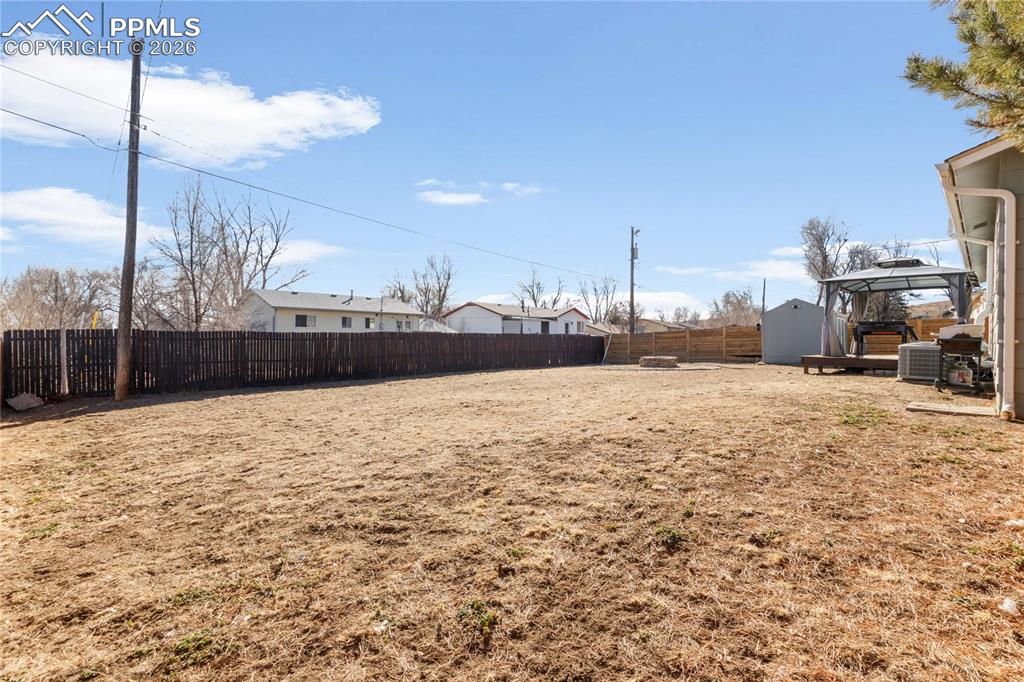 Fenced backyard with a gazebo, a residential view, and a storage unit