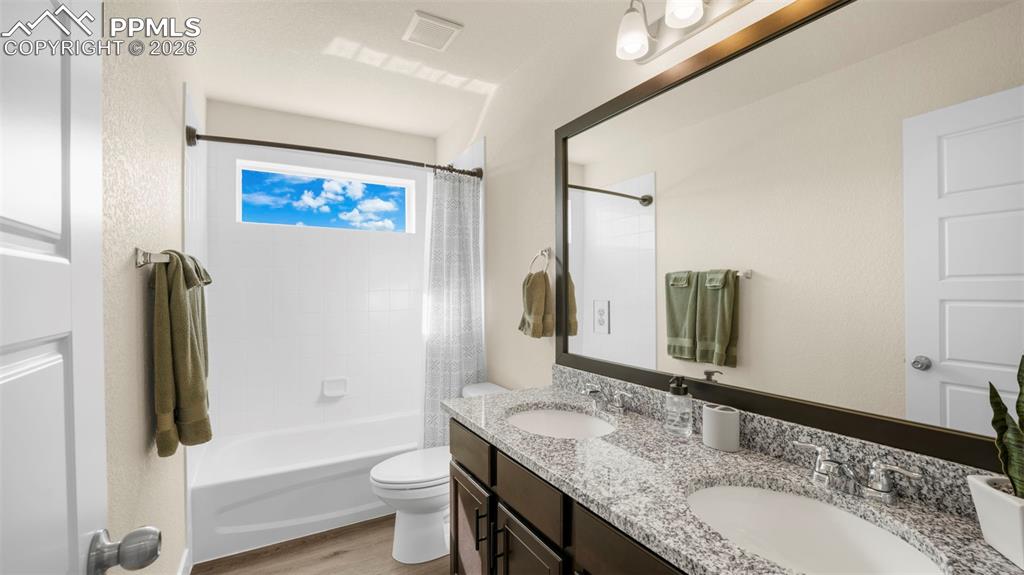 Full bath featuring double vanity, shower / bathtub combination with curtain, and light wood-style floors