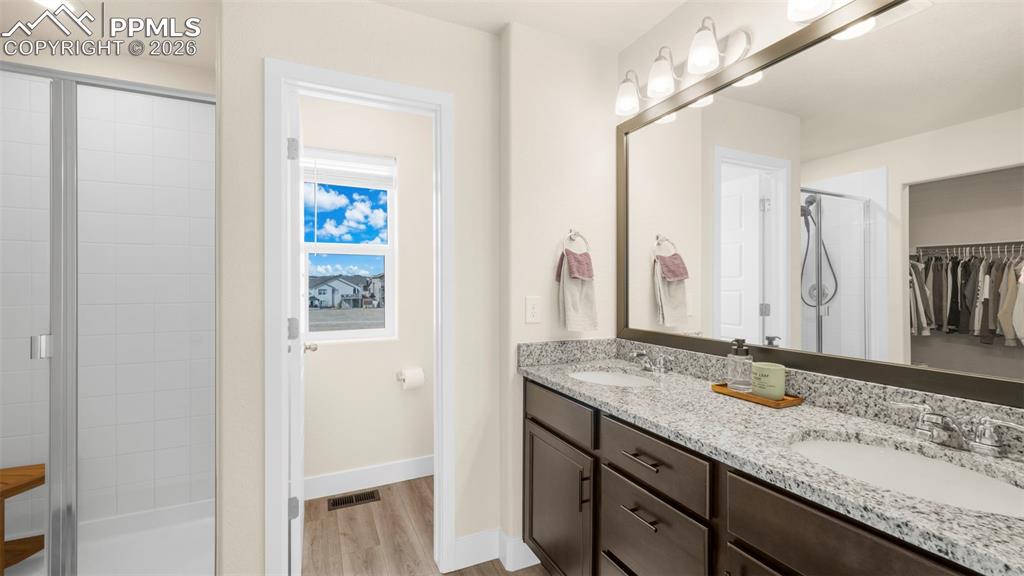 Full bathroom featuring double vanity, a walk in closet, a stall shower, and light wood-style floors