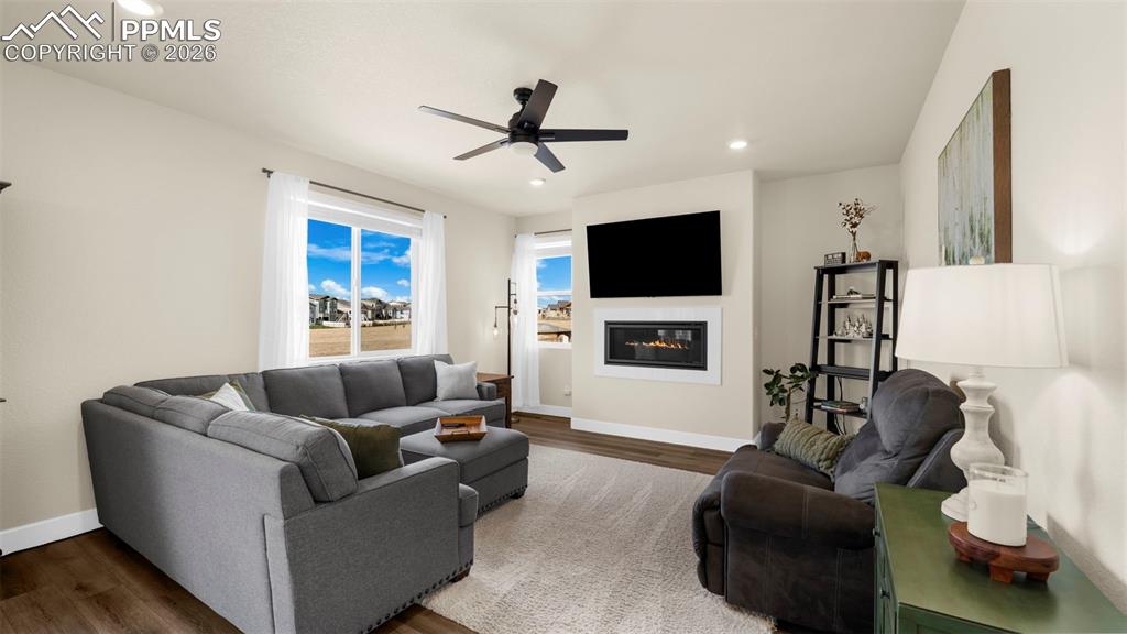 Living room featuring wood finished floors, a glass covered fireplace, ceiling fan, and recessed lighting