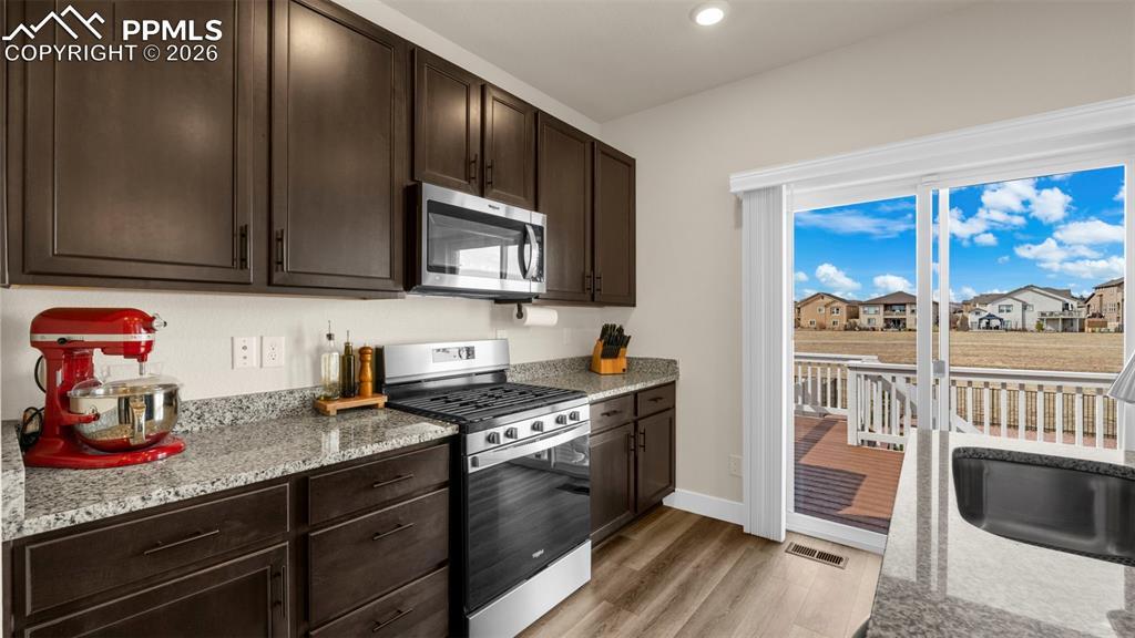 Kitchen with dark wood finish cabinets, stainless steel appliances, light stone counters, a residential view, and recessed lighting