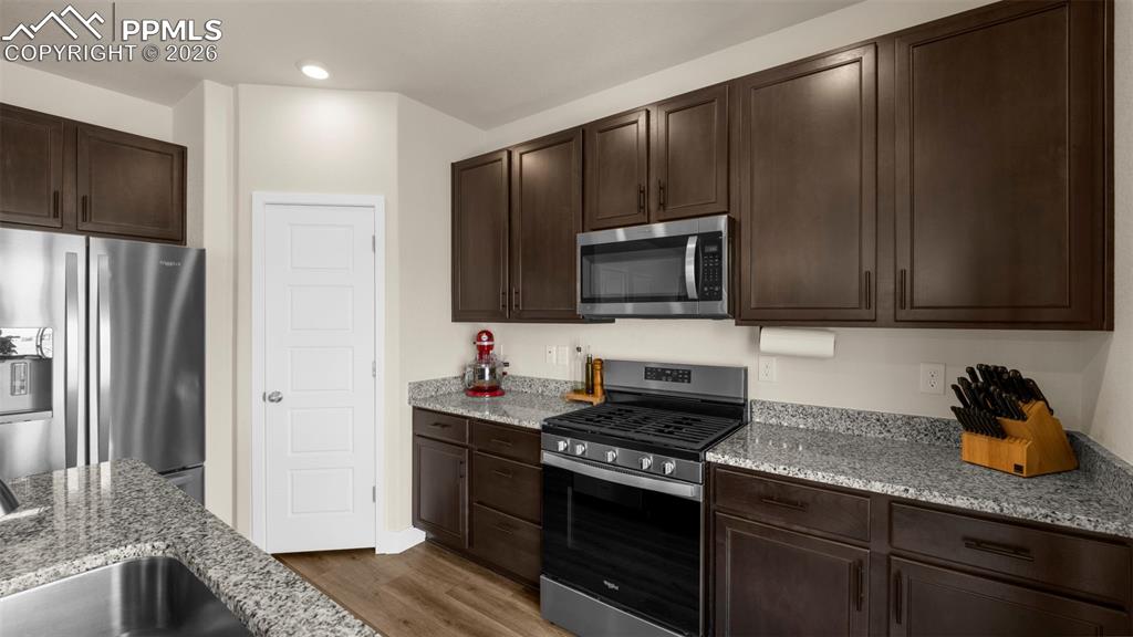 Kitchen featuring stainless steel appliances, dark wood finish cabinetry, and light stone counters