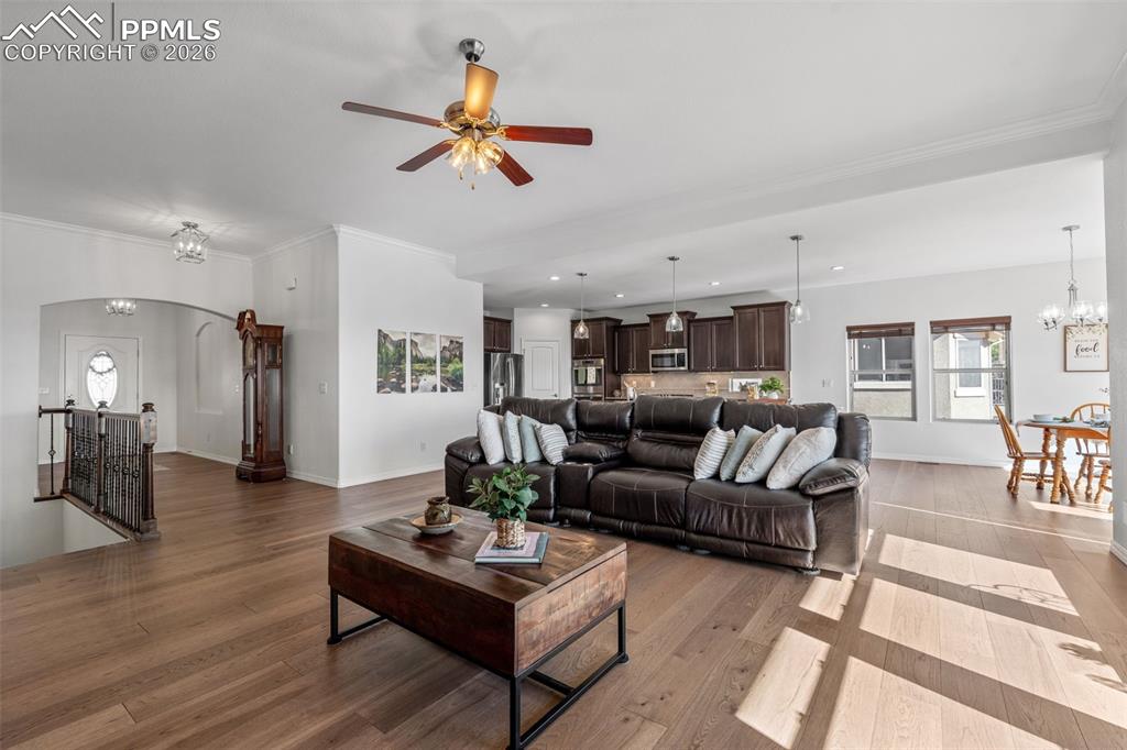 Living area featuring hanging lights, light wood-style flooring, a ceiling fan, arched walkways, and ornamental molding