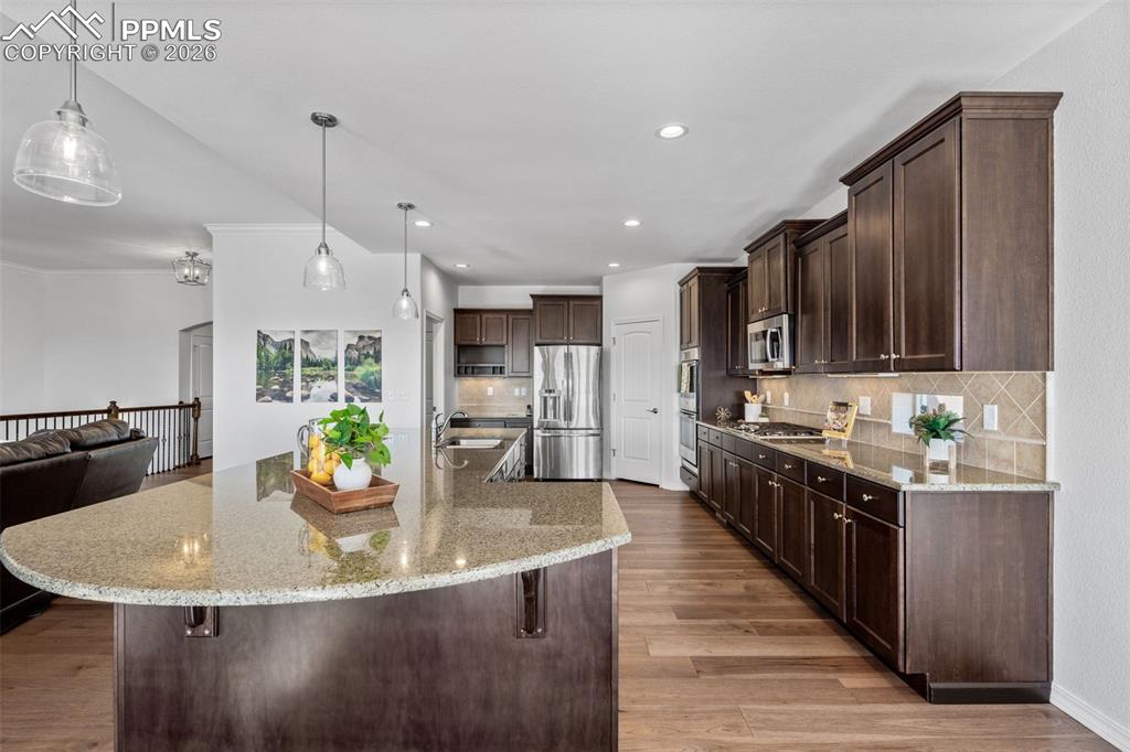 Kitchen featuring dark wood finish cabinets, light stone counters, stainless steel appliances, light wood-style flooring, and a large island