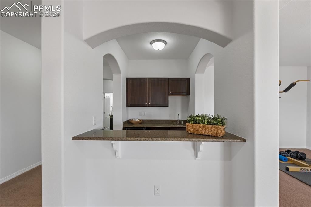 Kitchen with carpet flooring, dark wood finish cabinetry, a breakfast bar area, and dark stone countertops