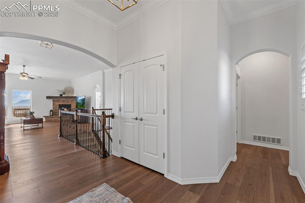 Hallway featuring arched walkways, dark wood-type flooring, ornamental molding, and an upstairs landing