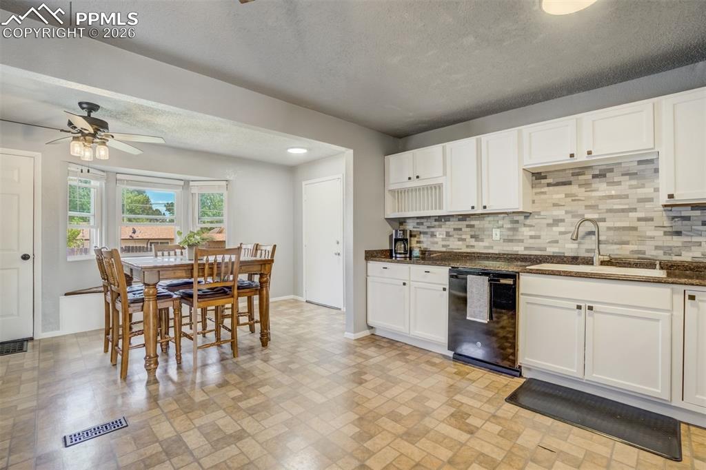 Kitchen with white cabinetry, dishwasher, a ceiling fan, dark stone countertops, and tasteful backsplash