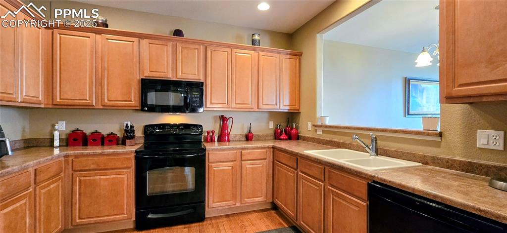 Kitchen featuring black appliances, light wood-style flooring, pendant lighting, and light countertops