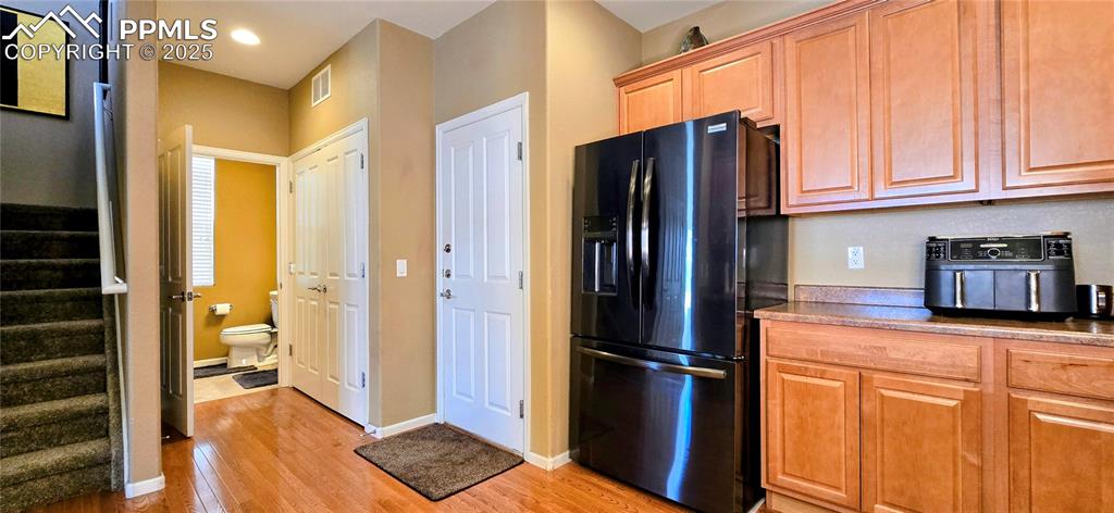 Kitchen with black refrigerator with ice dispenser, light wood-type flooring, light countertops, brown cabinets, and recessed lighting