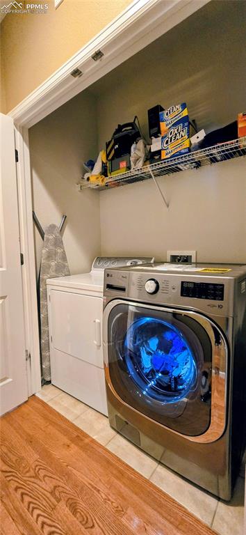 Washroom with light tile patterned flooring and washing machine and clothes dryer