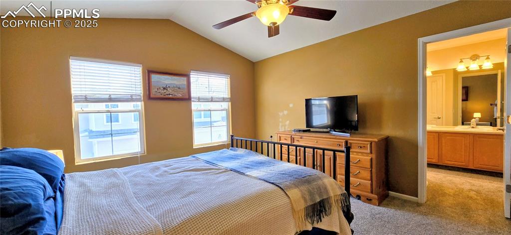 Bedroom featuring vaulted ceiling, light carpet, ensuite bathroom, and ceiling fan